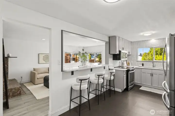 Open-concept kitchen and living connection at 4612 N 21st St, Tacoma, WA — featuring a spacious breakfast bar with modern seating, quartz countertops, stainless steel appliances, shaker cabinetry, and a bright pass-through overlooking the main living area. This North Tacoma home offers a functional and stylish layout perfect for entertaining, meal prep, and everyday living.