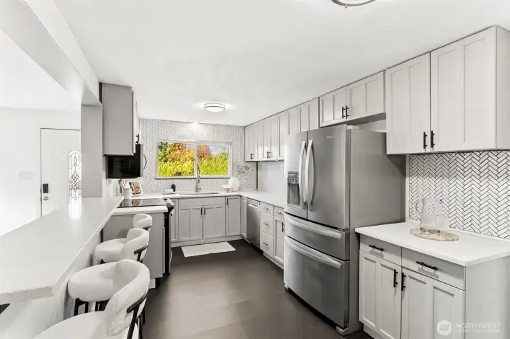 Bright, fully remodeled kitchen at 4612 N 21st St, Tacoma, WA — featuring sleek stainless steel appliances, quartz countertops, modern shaker cabinets, expansive storage, and a stylish herringbone tile backsplash. Large window provides natural light and backyard views. This North Tacoma home offers a contemporary, move-in-ready kitchen designed for cooking, entertaining, and everyday convenience.