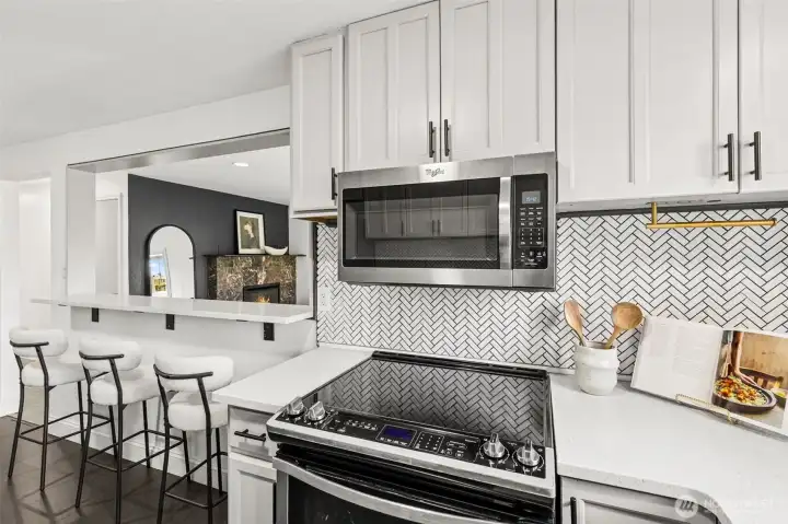 Beautifully updated kitchen at 4612 N 21st St, Tacoma, WA — featuring stainless steel Whirlpool appliances, smooth glass cooktop, quartz countertops, full herringbone tile backsplash, and a convenient breakfast bar overlooking the living room. This modern North Tacoma kitchen offers stylish finishes, functional design, and seamless flow perfect for cooking and entertaining.