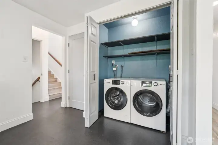 Convenient laundry area at 4612 N 21st St, Tacoma, WA — featuring a front-loading washer and dryer, built-in shelving, updated flooring, and a dedicated closet-style enclosure. This North Tacoma home offers functional and efficient laundry space with easy access to upstairs and downstairs living areas.
