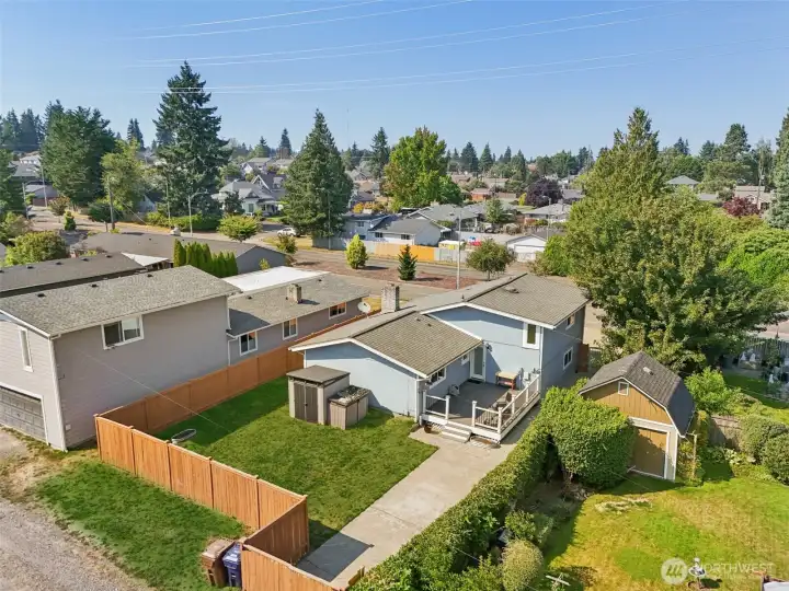 Aerial view of the backyard and exterior at 4612 N 21st St, Tacoma, WA — featuring a fully fenced yard, spacious deck, storage sheds, and extended driveway access. This North Tacoma home sits in a well-established neighborhood with tree-lined surroundings, offering privacy, outdoor living space, and convenient proximity to parks, schools, and local amenities.