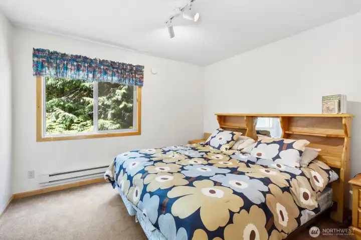Sunlit bedroom with large window and peaceful treetop views.