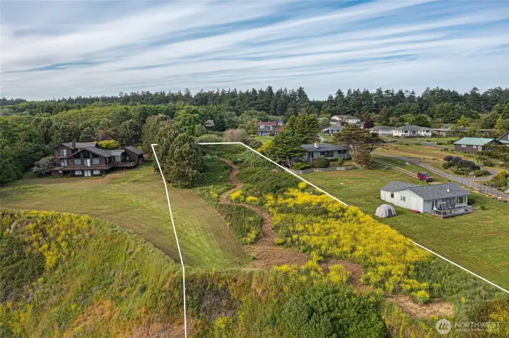 Property boundary view from the water side highlights the open acreage, natural wildflowers, and peaceful neighborhood setting near Eagle Cove.