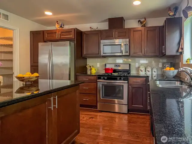 A chef's kitchen with stainless steel appliances and a gas range top for precision cooking. Also situated between two custom designed pantry spaces for easy overflow storage.