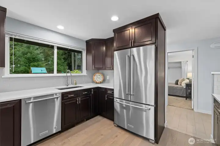 Modern kitchen with stainless steel refrigerator, dishwasher, and dark wood cabinetry, offering generous prep space and natural light.