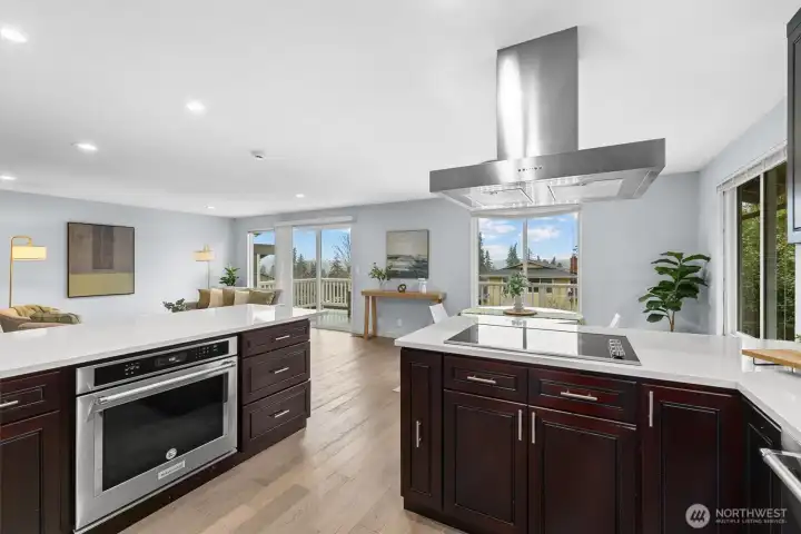Chef-inspired kitchen with massive island, quartz countertops, stainless range hood, and open sightlines to the living room and deck.