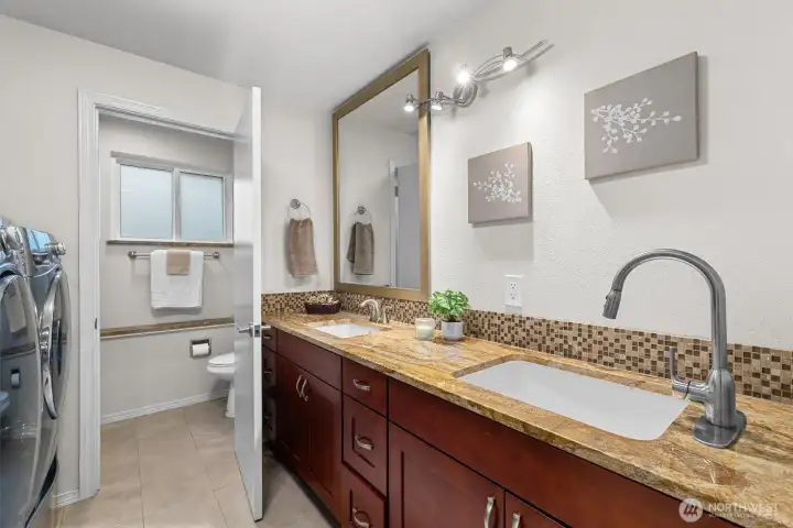 Updated bathroom with dual-sink vanity, generous counter space, and adjacent laundry area for added convenience.