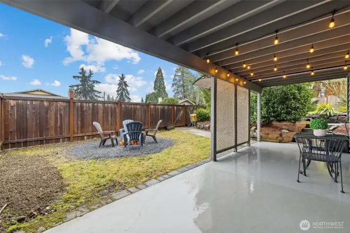 Covered patio overlooking the front yard, offering year-round outdoor living space with string lighting and room for seating.