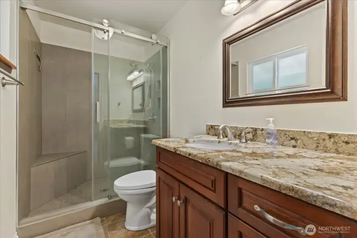 Upstairs primary ensuite with slab granite counters and a sleek, refined shower remodeled in 2024.