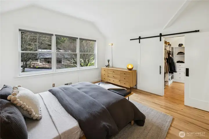 The upstairs primary suite is a serene retreat with vaulted ceilings and expansive windows overlooking the two-stall barn and grounds. Wake to peaceful pastoral views and enjoy the convenience of a generous walk-in closet tucked behind a modern barn door.