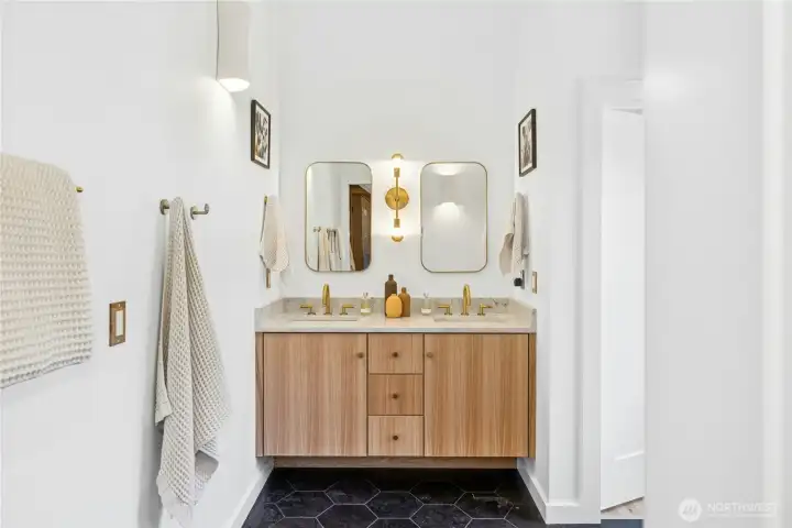 The spa-inspired primary bath features a custom double vanity with beautiful countertops, warm wood cabinetry, and designer brass fixtures. Clean lines and curated lighting create a fresh, elevated feel. Perfect for unwinding at the end of the day.