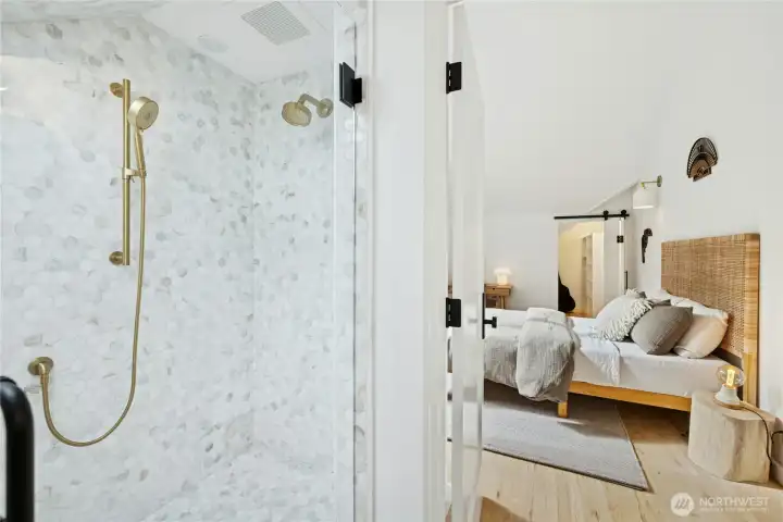 The newly added en suite bath features a stunning tile shower with designer brass fixtures and a skylight that pours in natural light. Paired with the vaulted bedroom just beyond, it creates a bright, private suite ideal for guests or everyday comfort.