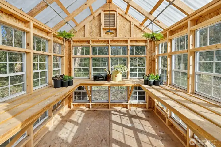 Charming greenhouse is filled with natural light and surrounded by windows, creating an ideal environment for year-round gardening and seedlings. With generous bench space and a peaceful woodland backdrop, it’s a dream setup for cultivating flowers, herbs, and homegrown produce.