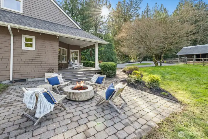 A paver patio with built-in fire pit extends the living space outdoors, framed by mature landscaping and a welcoming covered porch. Enjoy golden-hour gatherings with easy sightlines to the barn and fenced pasture. Perfect for entertaining while staying connected to the heart of the property.