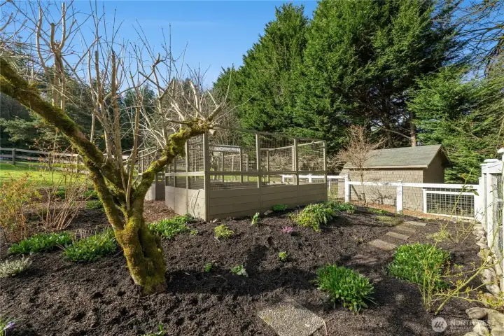 The garden area is thoughtfully laid out with established plantings, pathways, and an enclosed bed space for easy seasonal growing. An irrigation system on a timer supports low-maintenance care, making it easy to cultivate fresh produce and flowers in a private, country setting.