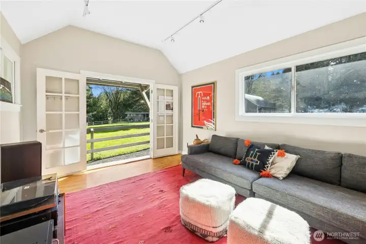 Inside the heated bonus studio, vaulted ceilings and abundant natural light create a comfortable, flexible room for an office, studio, or lounge. French doors open directly to the pasture, making it an ideal hub for equestrian use, hobbies, or a quiet retreat.