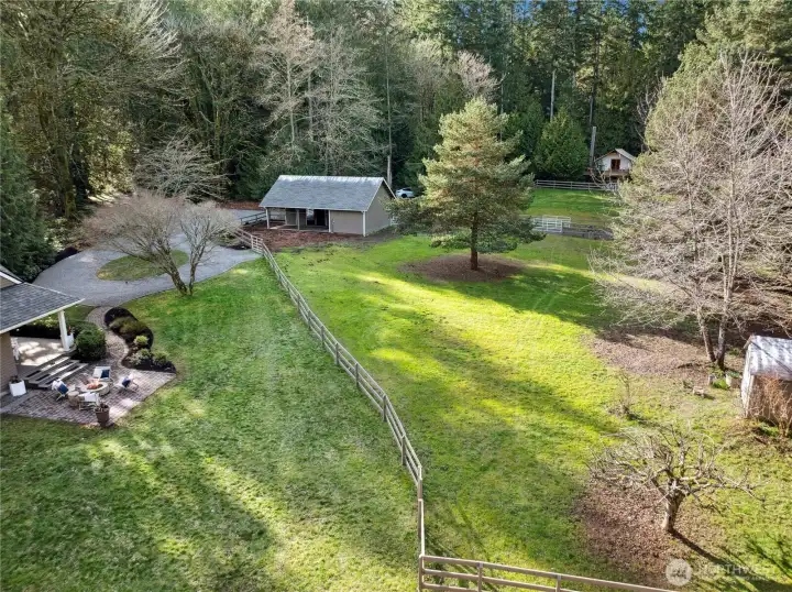 An aerial view captures the property’s open, usable acreage with fenced paddock areas, the two-stall barn, and the main home perfectly positioned for privacy. The expansive lawn and mature trees create a serene setting, offering room to ride, graze, and enjoy the land in every season.