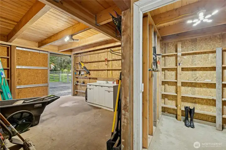 Inside the barn, the well-organized interior offers generous workspace, built-in shelving, and a utility sink to support daily chores. A dedicated tack room to the right provides secure, convenient storage for gear, making barn management efficient and streamlined.