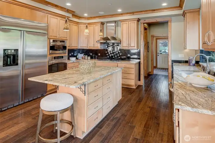The kitchen is both beautiful and highly functional. Rich wood cabinetry, granite countertops, and a striking tile backsplash create a warm, grounded feel, while stainless appliances and a generous island make everyday cooking feel easy.