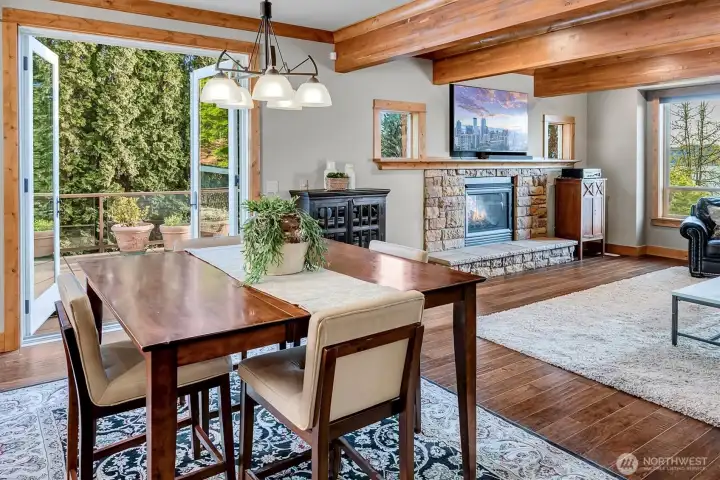 The eating space blends seamlessly into the family room, framed by exposed beams and anchored by a stone fireplace. French doors lead out to the deck, extending the living space outdoors.