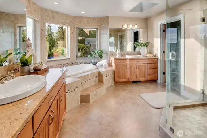 The primary bath is spacious and thoughtfully designed, with dual vanities, abundant counter space, and warm stone finishes throughout. Natural light fills the room.