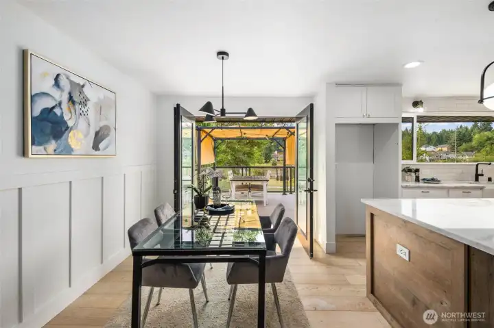 The dining room is centered beneath a sleek modern chandelier and opens through wood-framed French doors showcasing large glass panes to the expansive view deck, where glimpses of Hilton Lake create a stunning backdrop for every meal