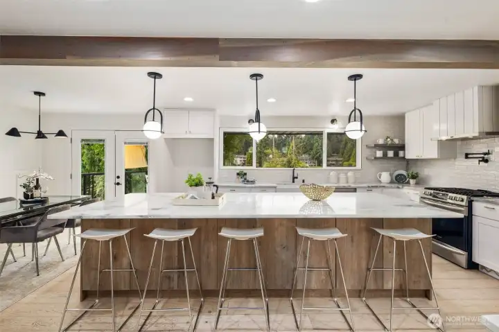 The centerpiece of the kitchen is an expansive quartz-slab island with abundant seating, convenient outlets, and extensive storage cabinetry. Overhead, modern black-framed pendant lights with glowing globe shades add a sophisticated touch, perfectly complementing the island’s elegant design.