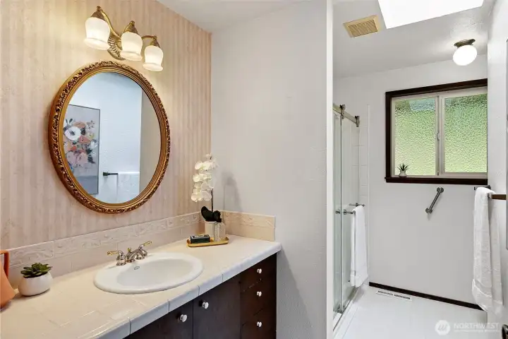 A main level bath includes a large, remodeled shower, a skylight, and a tiled vanity.