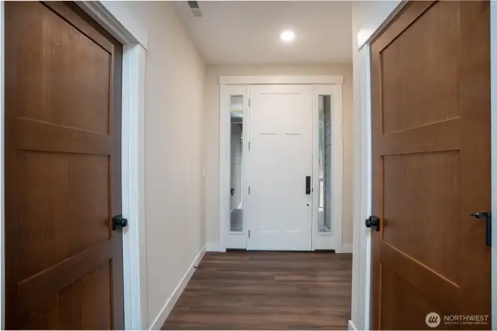 View back to the entry with side lights flanking the main door.  Interior door are solid wood in a stained finsih accented by black hardware.