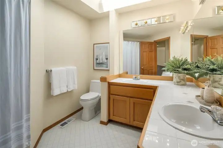Larger hall bathroom with dual sinks, skylight, and shower over the bathtub