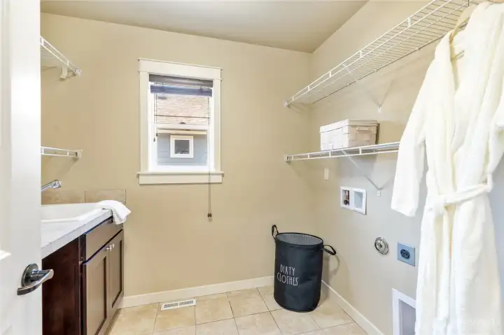 Convenient upper-level laundry with utility sink, cabinets, and shelving.