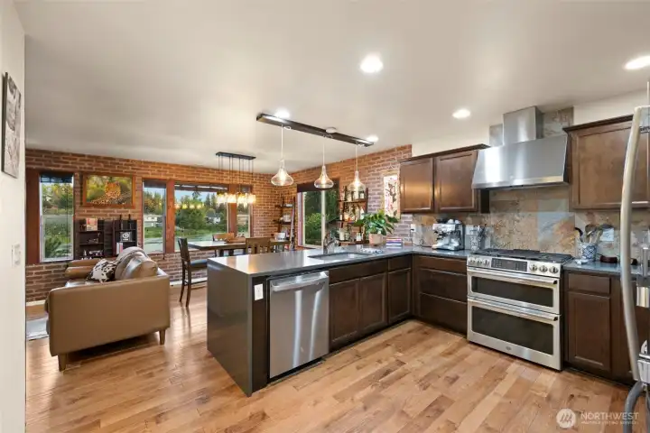 Elevate your culinary experience in this sophisticated open-concept kitchen, where sleek stainless-steel appliances — including a gas cooktop and double oven — pair beautifully with rich custom cabinetry and polished solid-surface countertops. Brazilian hardwood floors and striking exposed brick walls set a refined tone, while expansive windows frame tranquil lake views that make every meal feel like a retreat.