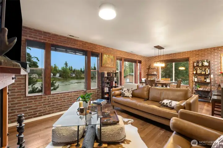 Framed by expansive windows, this inviting living and dining area is designed to celebrate the lake views and natural light that define the home. Thoughtful open-concept design allows the spaces to flow effortlessly together — ideal for everything from casual weeknight dinners to elegant gatherings with friends. Warm wood floors and custom brick veneer detailing complete the space with timeless character and elevated style.
