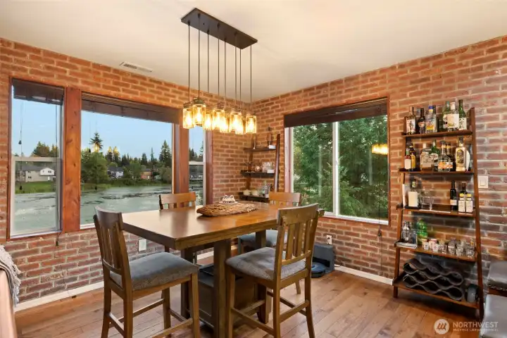 Enjoy memorable meals with a view in this light-filled dining space, where expansive windows showcase tranquil lake scenery and surrounding evergreens. Warm wood floors and custom brick veneer detailing create an inviting, elevated atmosphere, while designer lighting adds a touch of modern elegance. Whether it’s casual breakfasts or special celebrations, this space is designed for gathering and connection.