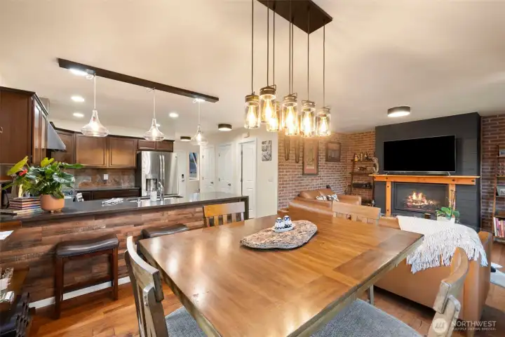 This open-concept main level is designed for effortless everyday living and seamless entertaining. From casual breakfasts at the oversized dining table to lively evenings gathered around the fireplace, the thoughtful layout ensures every space feels connected. Designer lighting, rich wood tones, and custom brick veneer walls add warmth and character, while the central kitchen island anchors the room as both a functional workspace and a natural gathering spot.