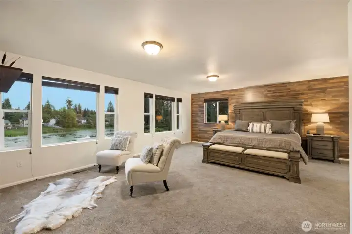 Spacious and serene, the primary suite offers a true retreat from the everyday. The generous proportions of the room — easily accommodating a king-sized bed with plenty of space to spare — create a sense of openness and comfort. Expansive windows flood the space with natural light and capture calming lake views, while the warm wood accent wall adds texture and timeless character.