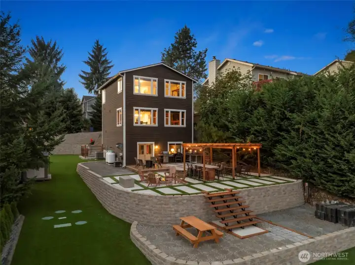 Evening ambiance highlights the layered outdoor design — multiple entertainment zones, easy access to the water, and a seamless indoor-outdoor connection.