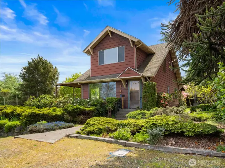 Lush greenery surrounds this charming corner-lot home, highlighting its storybook curb appeal and peaceful North Tacoma setting near Point Ruston and Puget Sound.