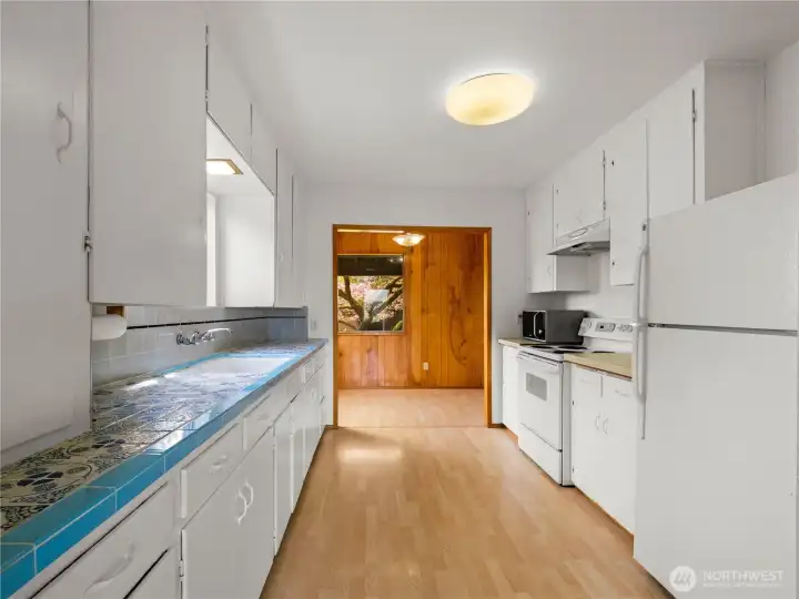 Bright kitchen features beautiful tile countertops, blending vintage charm with a fresh, inviting space at the heart of the home.