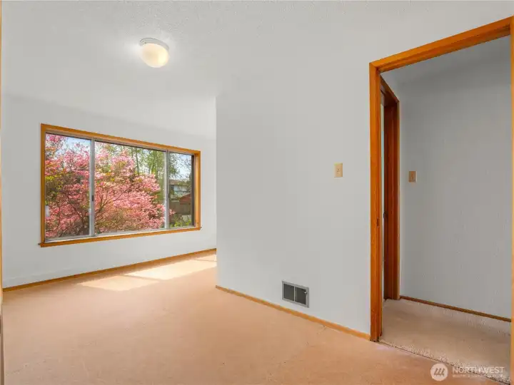 Second bedroom features large windows that beautifully frame the lush garden and surrounding landscaping, filling the space with natural light and a peaceful view.