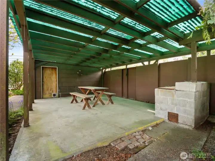 Covered area off the garage provides a cozy backyard retreat, perfect for relaxing or entertaining while enjoying the surrounding mature landscaping.