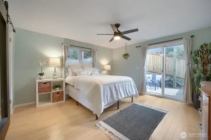 Primary bedroom with mirrored barn door to walk-closet with organization racks, ceiling fan with light, window that overlooks back deck and slider to its own private deck