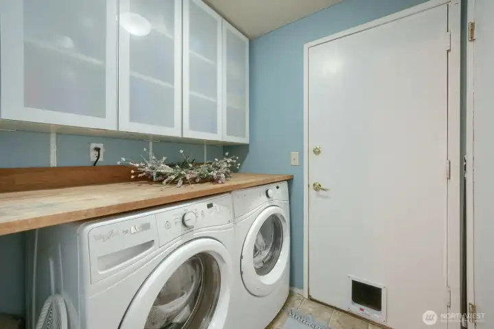 Laundry room off garage features chic, built-in glass cabinets, front loading whirlpool W/D & a contemporary, butcher block style countertop for easy sorting and folding straight out of the dryer.