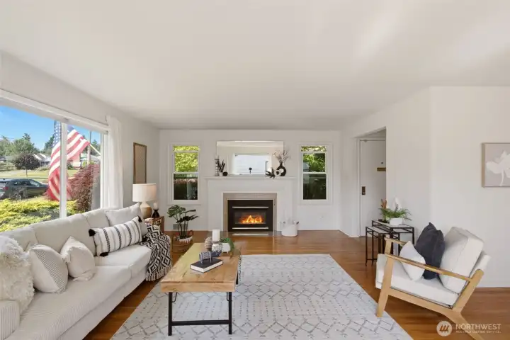 Enter into a spacious and light-filled living room featuring large windows and a gas fireplace