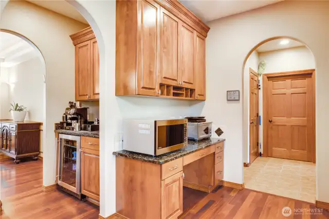 A butler's pantry, accompanied by a walk-in pantry located across the hallway, serves as an excellent coffee station, bar, or transition to the dining room. A built-in desk area provides additional storage options. The curved architectural details throughout this home add a touch of elegance and visual interest to these spaces. The door to the right is for the laundry and the main floor bedroom and bathroom are just to the right.