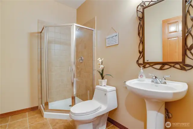 This bathroom on the main floor features tile flooring throughout, a walk shower, and a pedestal sink.