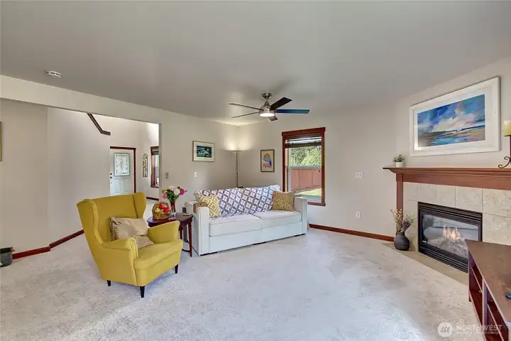Bright and inviting living room featuring a cozy fireplace and a new ceiling fan for comfort. All-new lighting throughout the home adds a fresh, modern touch. The open floorplan flows seamlessly into the kitchen and dining areas.