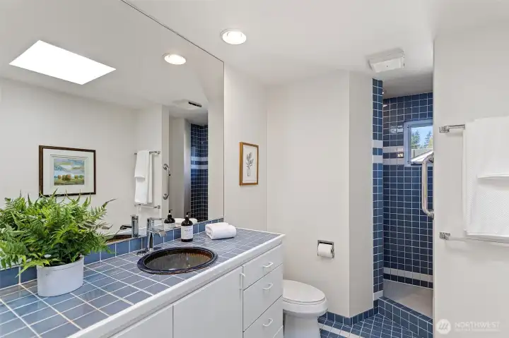 . En-suite bathroom with skylight. Private walk-in shower featuring seating, wall mounted rain shower, a shampoo nice and opening window,  beautiful tilework continues, custom vanity sink and wall mounted  vanity faucet.