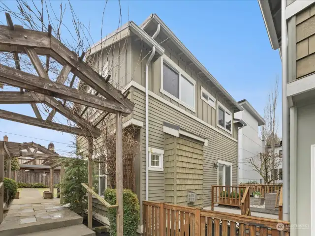 This shows the back of the home and the fence to the patio and deck. The walkway has cascading arbors with climbing flowering vines