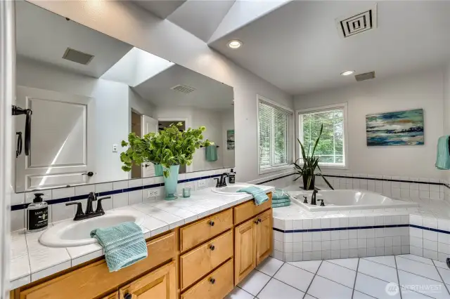 Primary bath with double sinks, jetted tub, skylight, and crisp white tile.